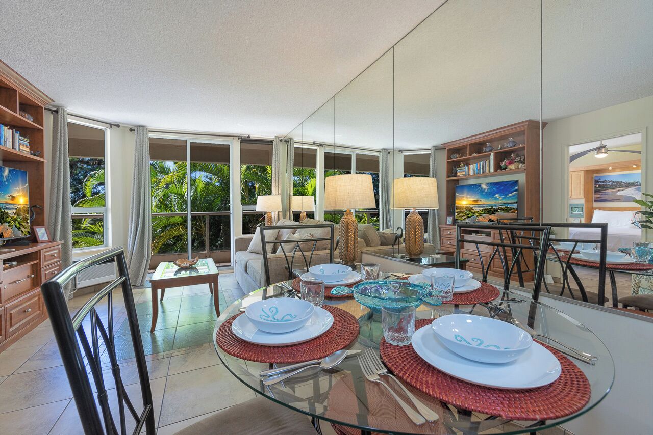 A spacious dining area with a glass table, red placemats, and a view of lush greenery outside.