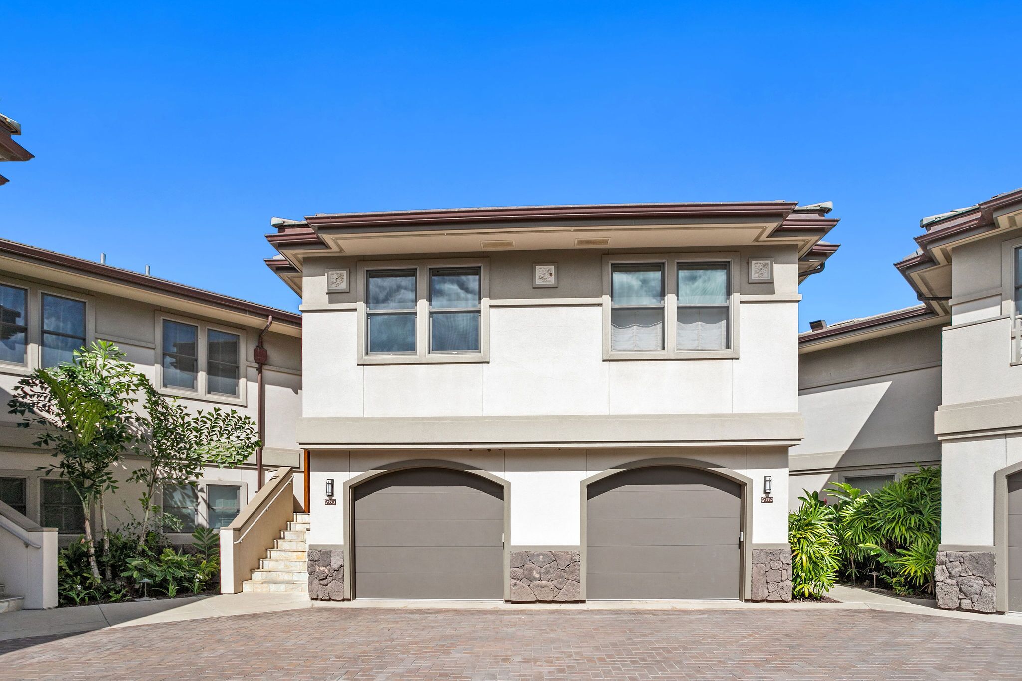 A modern two-story house with a central garage, a staircase, and a well-maintained garden.