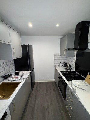 A modern kitchen with white cabinets, a black refrigerator, a stove, and a microwave. - Modern 2 Bed Apartment, Close to Gla Airport & M8 (Paisley)