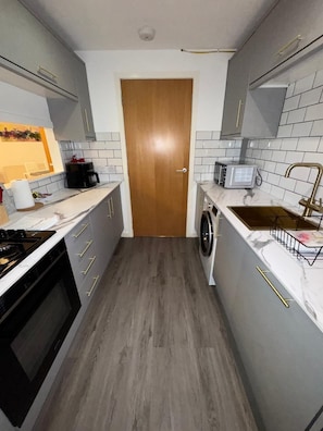 A compact kitchen with a microwave, coffee maker, and a washing machine. - Modern 2 Bed Apartment, Close to Gla Airport & M8 (Paisley)
