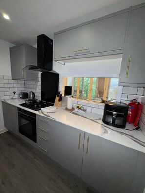 A modern kitchen with grey cabinets, a black stove, and a coffee maker. - Modern 2 Bed Apartment, Close to Gla Airport & M8 (Paisley)