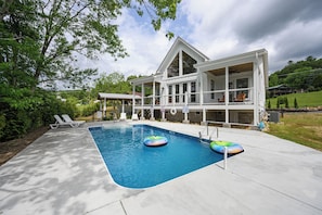Uma área de piscina com espreguiçadeiras, uma casa ao fundo e um céu nublado.
