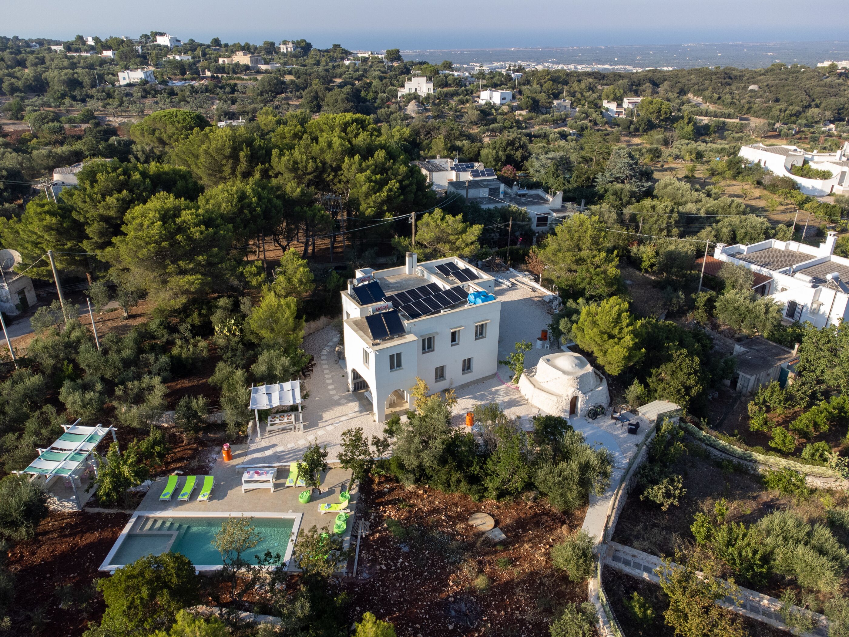Ett flygbildsbild av ett bostadsområde med ett hus som har solpaneler, en swimmingpool och en trädgård.