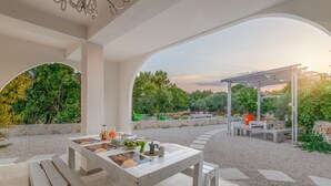 Un patio exterior con una mesa lista para comer, rodeado por una pérgola y follaje.