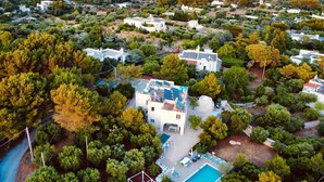 Vista aérea de una zona residencial con una casa grande, piscina, abundante vegetación y un paisaje costero.