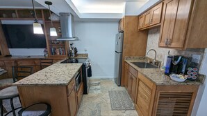 A modern kitchen with wooden cabinets, a granite countertop, a built-in oven, a stainless steel sink, and a coffee machine. - Beachfront Condominium with Private Beach Access and Heated Pool (South Padre Island)