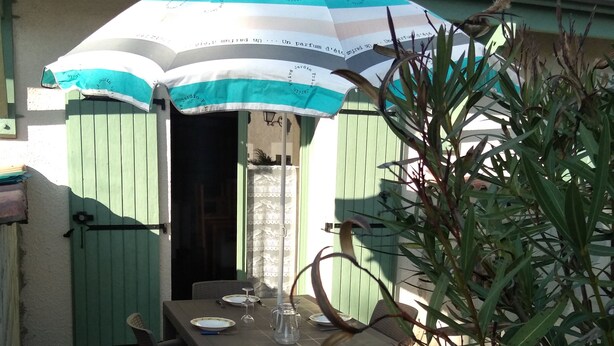 Uma área de refeições ao ar livre com uma mesa posta para dois, um guarda-sol e uma porta verde.