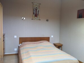 Une chambre à coucher avec un lit, une table de chevet en bois, une lampe fixée au mur et une tapisserie.