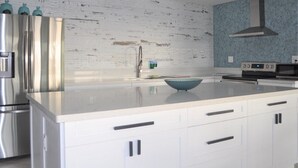 A modern kitchen with white cabinetry, a stainless steel refrigerator, a blue bowl on the counter, and a backsplash with a blue pattern. - Paradise Moon Bay! (Key Largo)