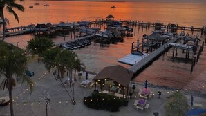 A marina at sunset with boats docked, a beach area with lounge chairs, and a small structure with string lights. - Paradise Moon Bay! (Key Largo)