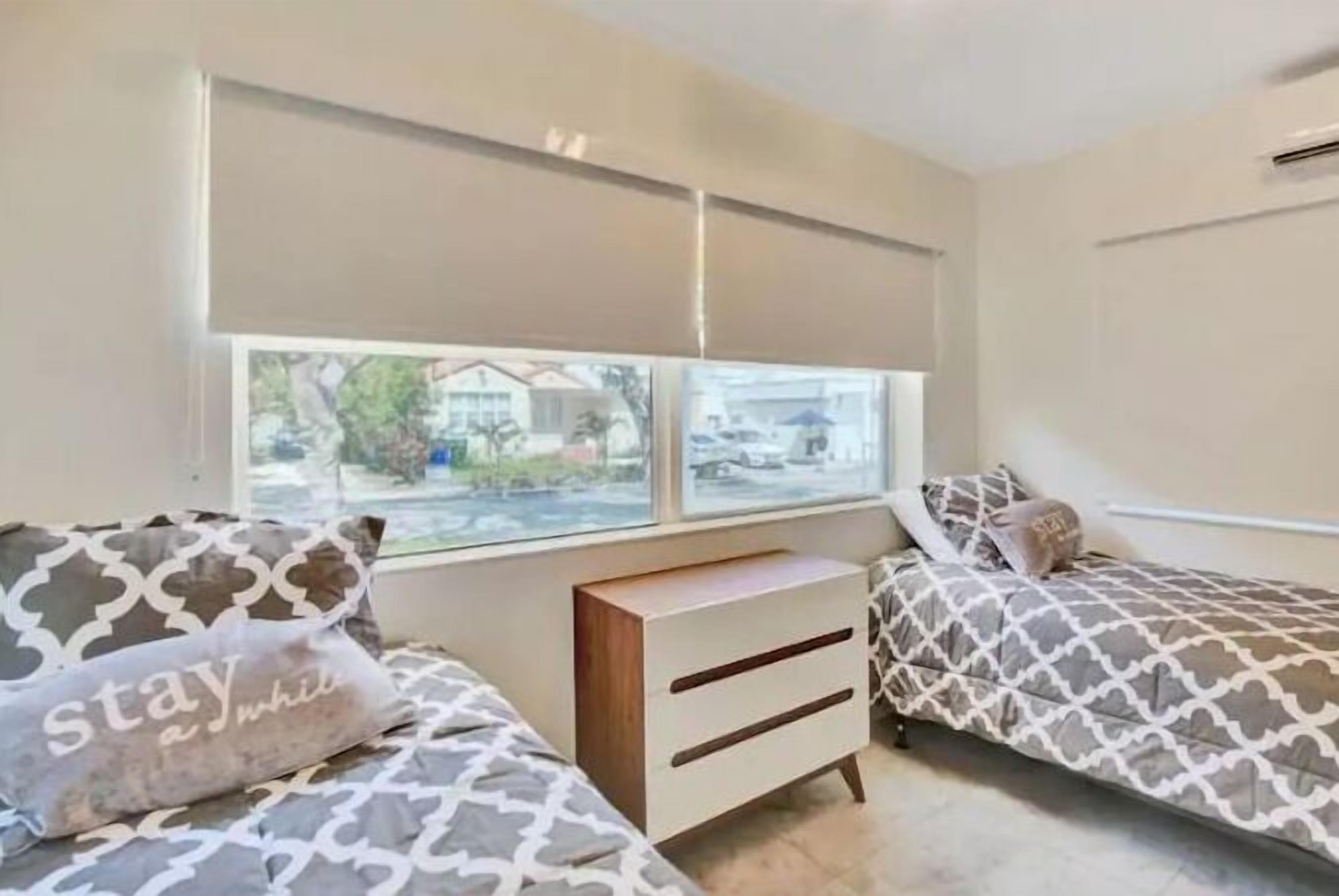A bedroom with two beds, a nightstand, and a window with blinds.
