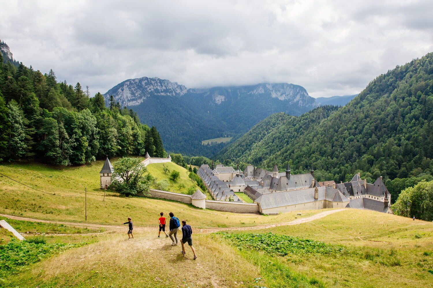 Un ensemble de bâtiments historiques formant un château, entouré de collines et de montagnes verdoyantes.