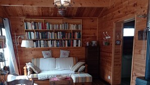Interior acogedor de una cabaña con techo de madera, un sofá, una estantería, una mesa de comedor y un estufa de leña.