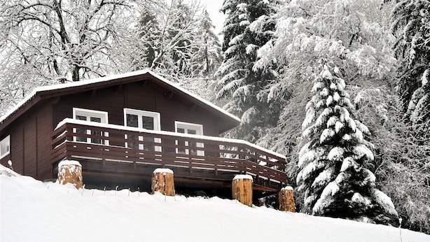 Una cabaña de madera con balcón, rodeada de árboles cubiertos de nieve.