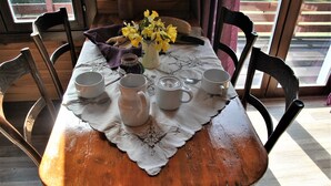 Una mesa de madera con mantel de encaje, tazas de cerámica blanca, una tetera y un florero con flores amarillas.