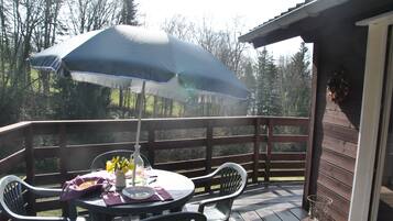 Une terrasse en bois avec une table et des chaises, un grand parasol et un vase rempli de fleurs.