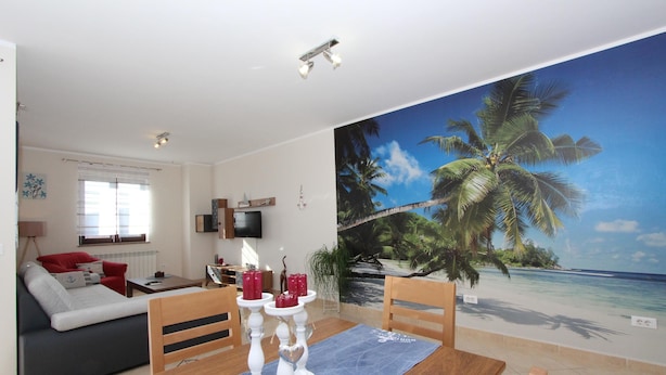 Una sala de estar con un gran mural de playa, una mesa de comedor con velas y un sofá con cojines rojos.