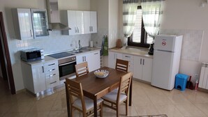 Una cocina compacta con armarios blancos, un microondas, un horno y un lavamanos. Hay una mesa de comedor con sillas y un cuenco decorativo encima.