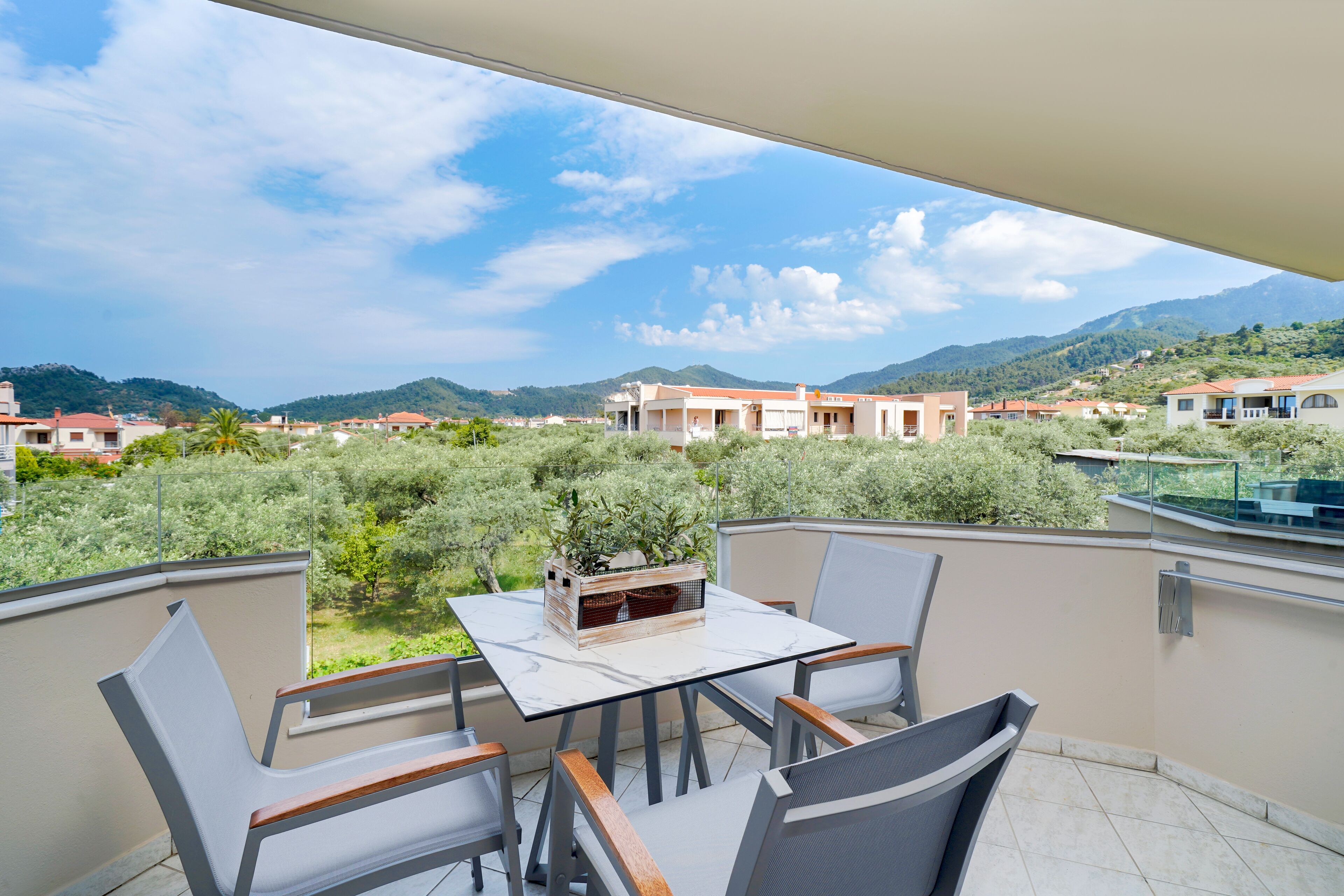 Un balcon avec une table et des chaises, donnant sur un quartier résidentiel avec des maisons et de la verdure.