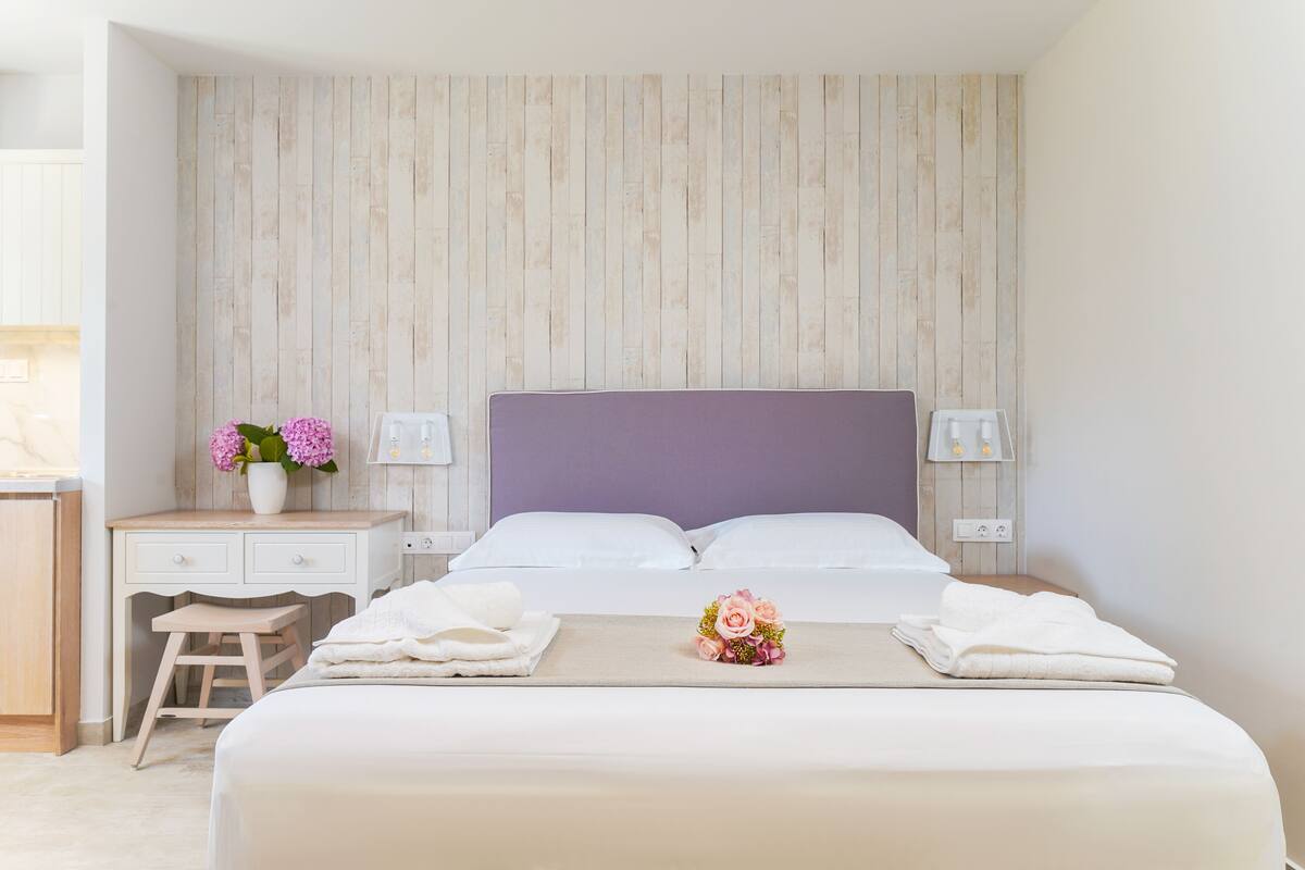 Une chambre à coucher bien rangée, avec un lit, des tables de chevet, une petite table de nuit et un petit tabouret.