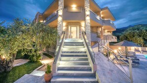 A modern multi-story building with a central staircase, outdoor pool, and surrounding greenery.