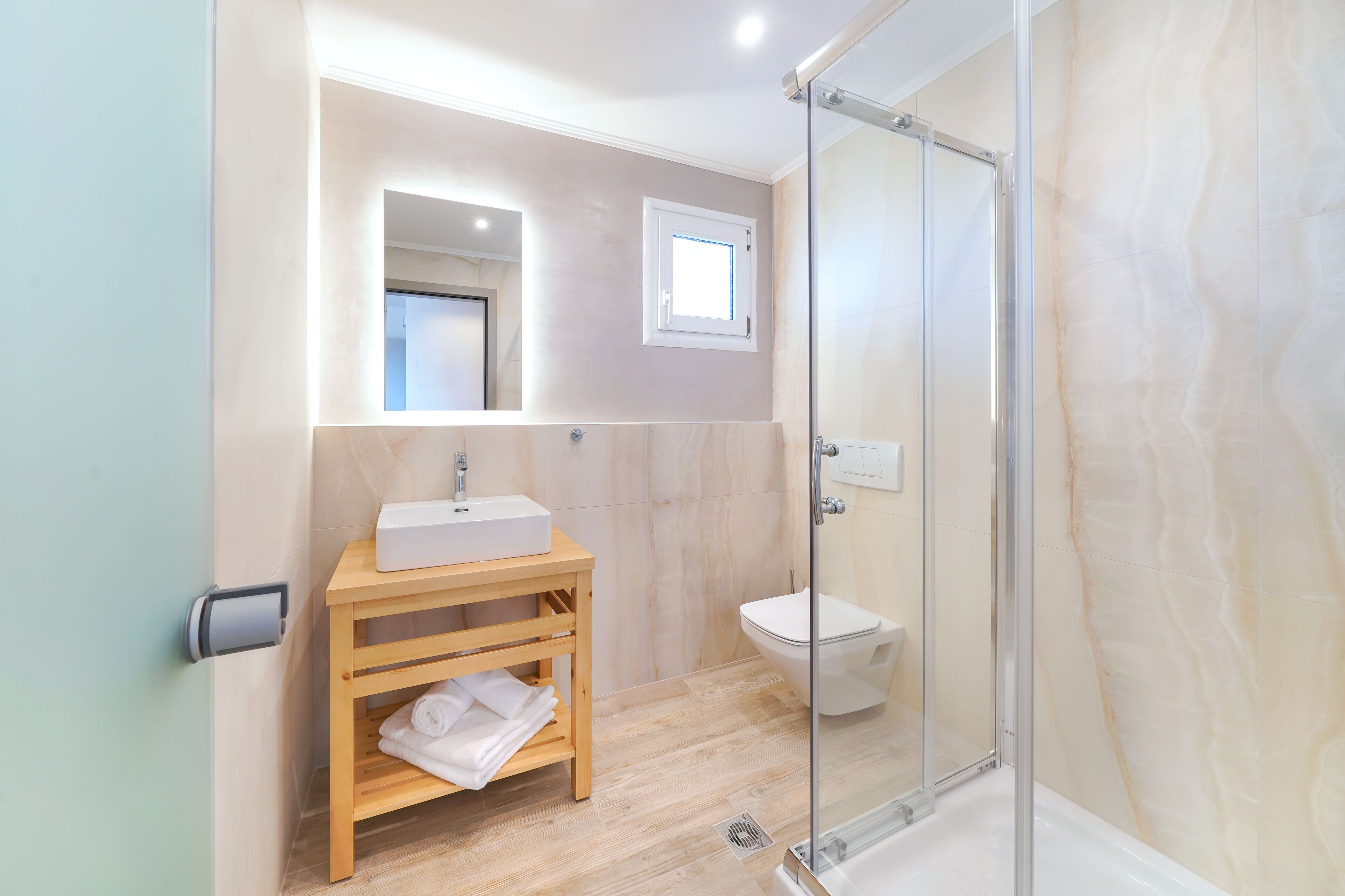 A modern bathroom with a glass-enclosed shower, a wooden vanity with a sink, and a toilet.