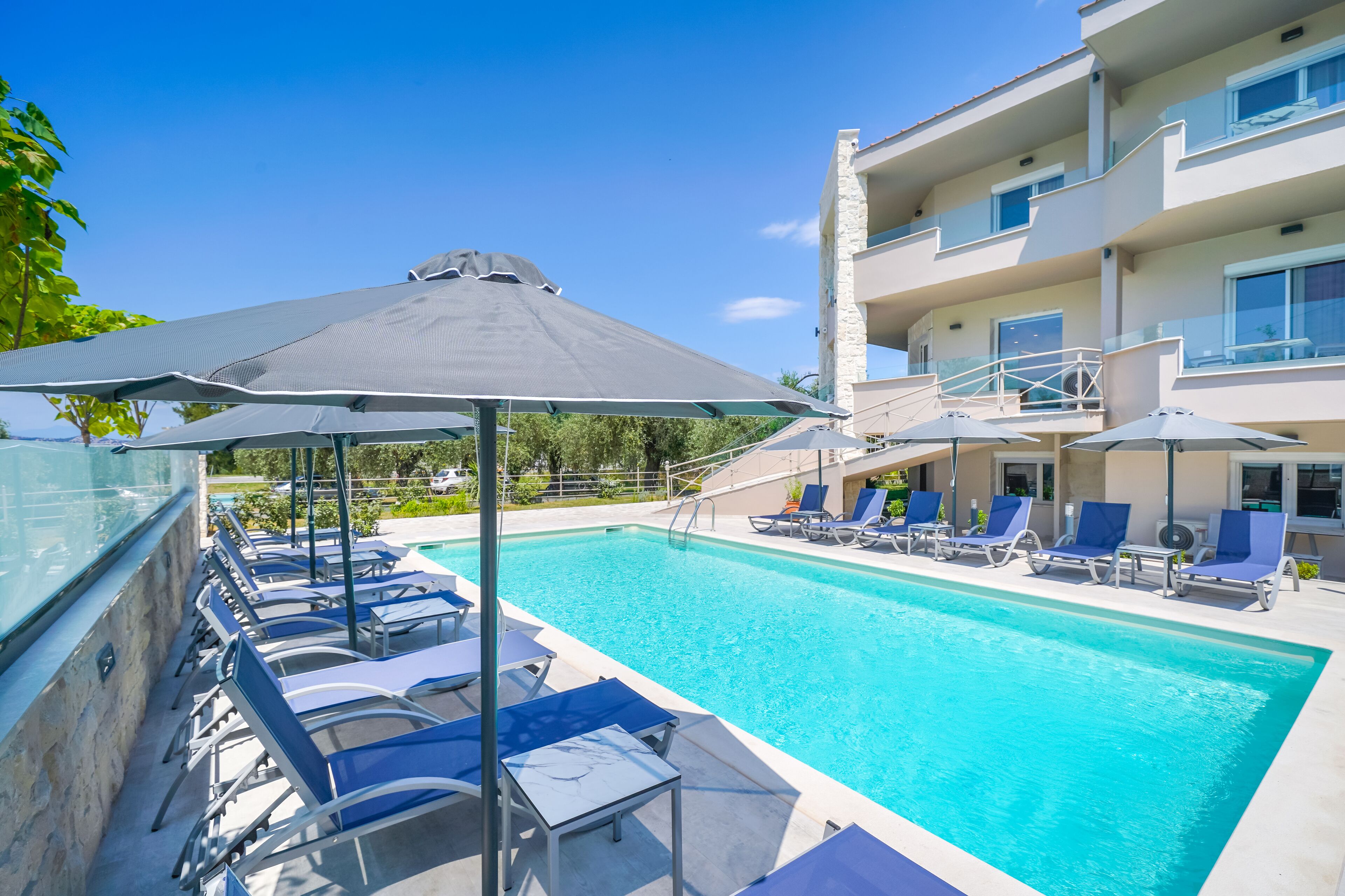 Una piscina con sillones de descanso y sombrillas, rodeada por un edificio con balcones.