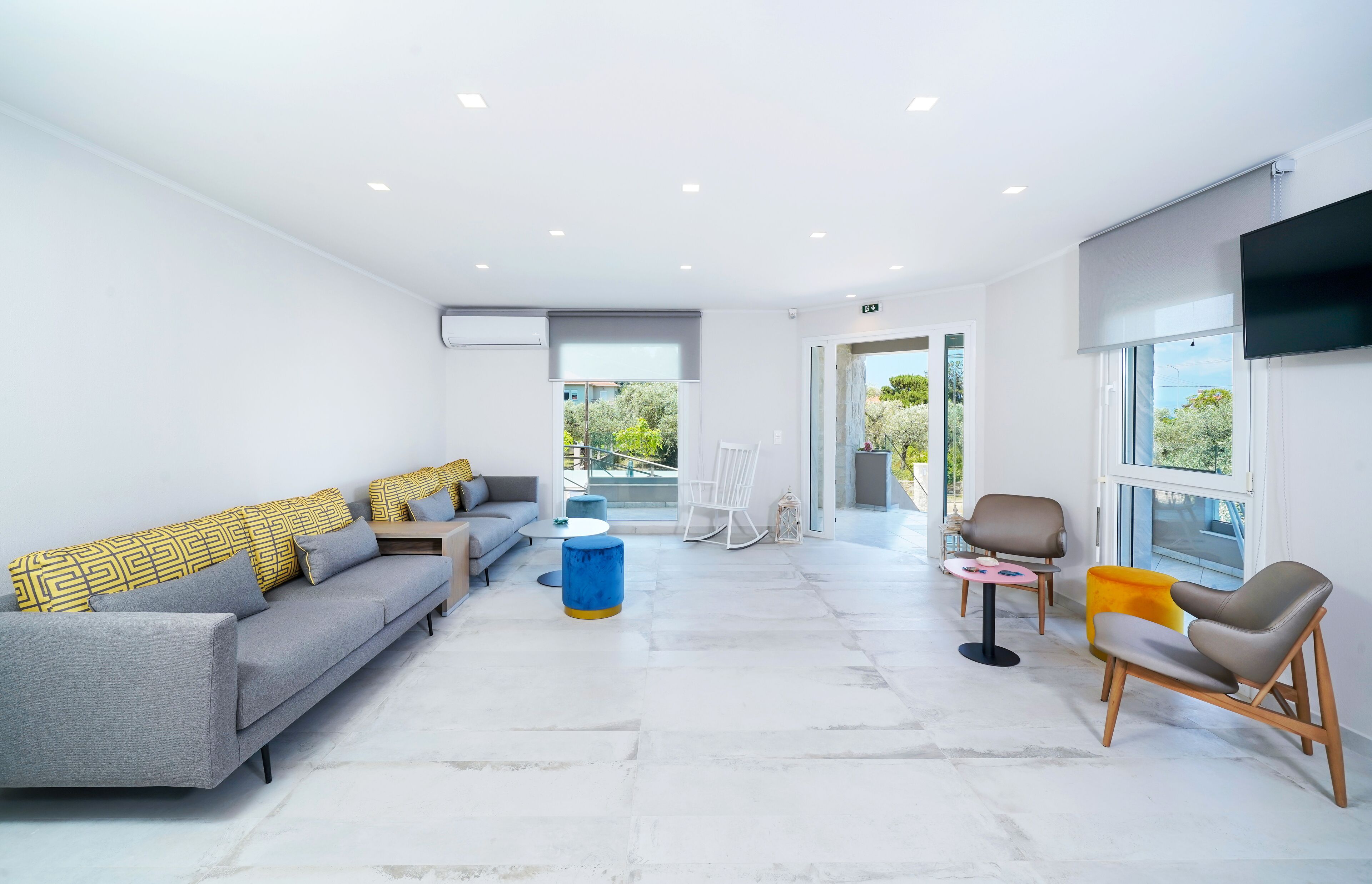 A modern living room with a grey sofa, a blue ottoman, and a white rocking chair.