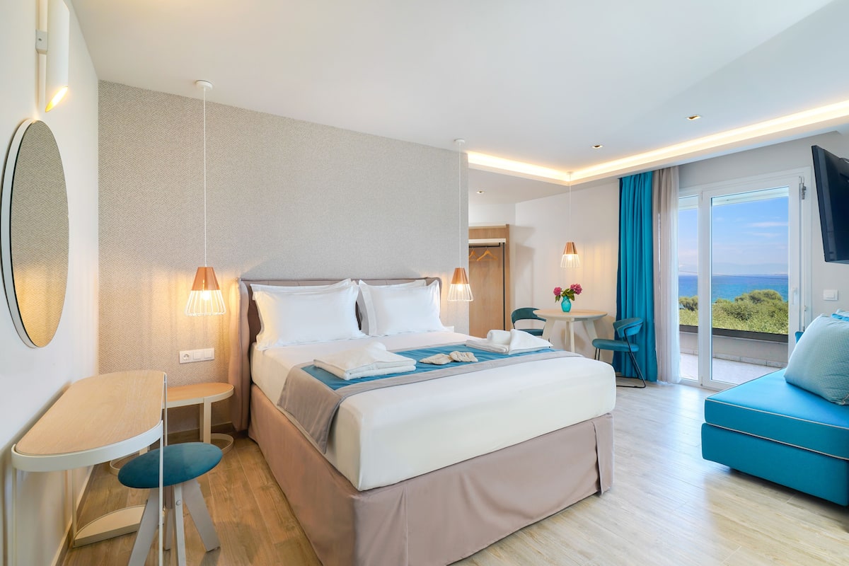 Une chambre d’hôtel moderne équipée d’un lit, de tables de chevet, d’un petit bureau, d’une chaise, d’un canapé et d’un téléviseur.