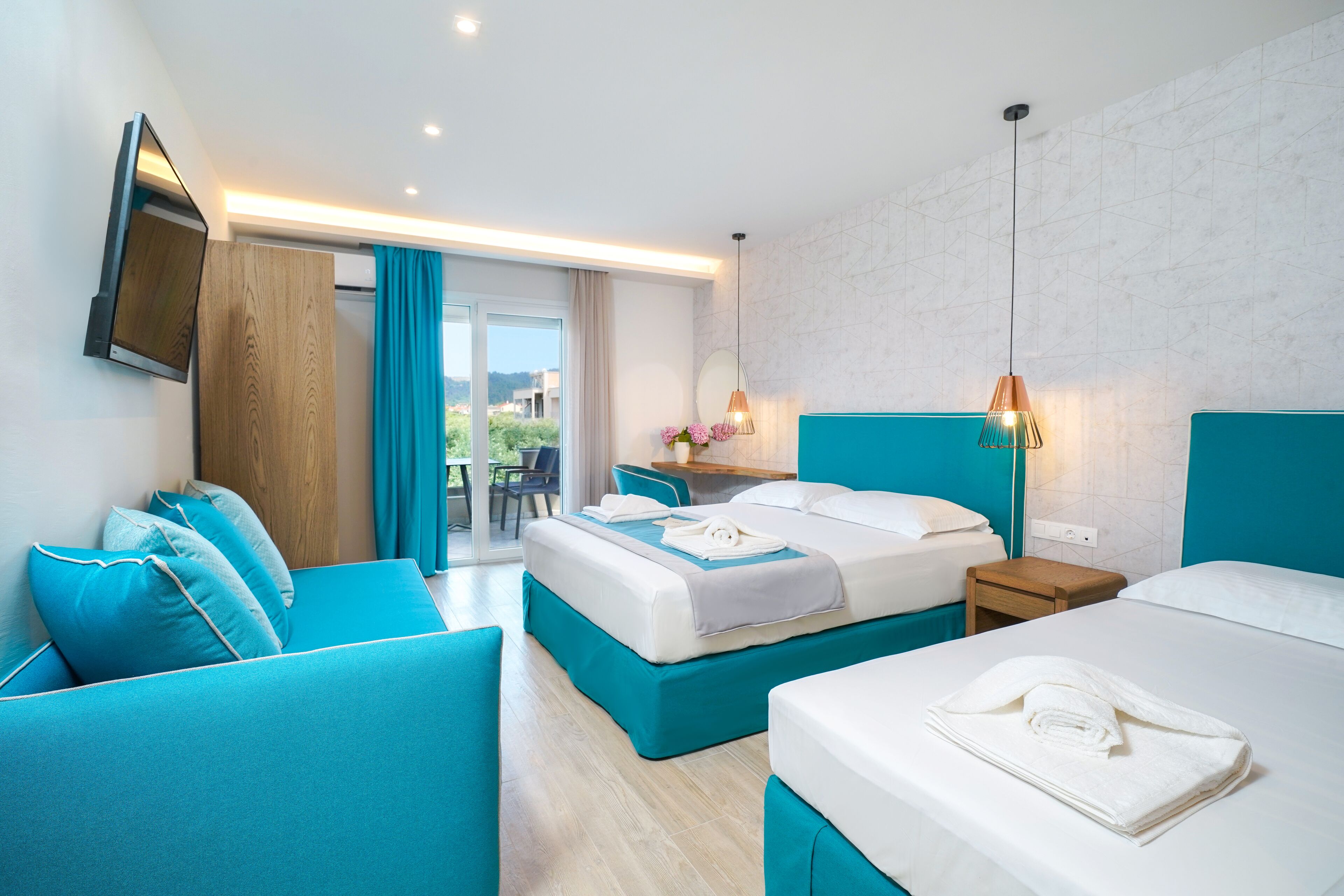 Ein Hotelzimmer mit zwei Betten, einem Sofa, einem kleinen Tisch und einem an der Wand befestigten Fernseher.