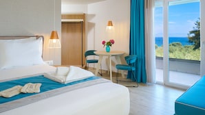 A hotel room with a bed, a table with chairs, a vase with flowers, and a view of the sea.