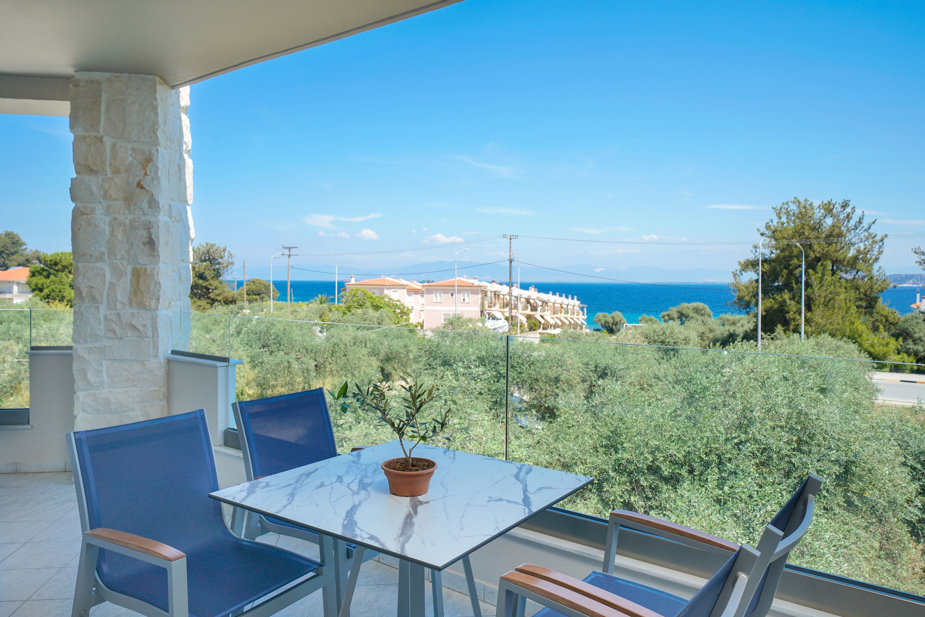 A balcony with a table and chairs, overlooking a coastal area with buildings and trees.