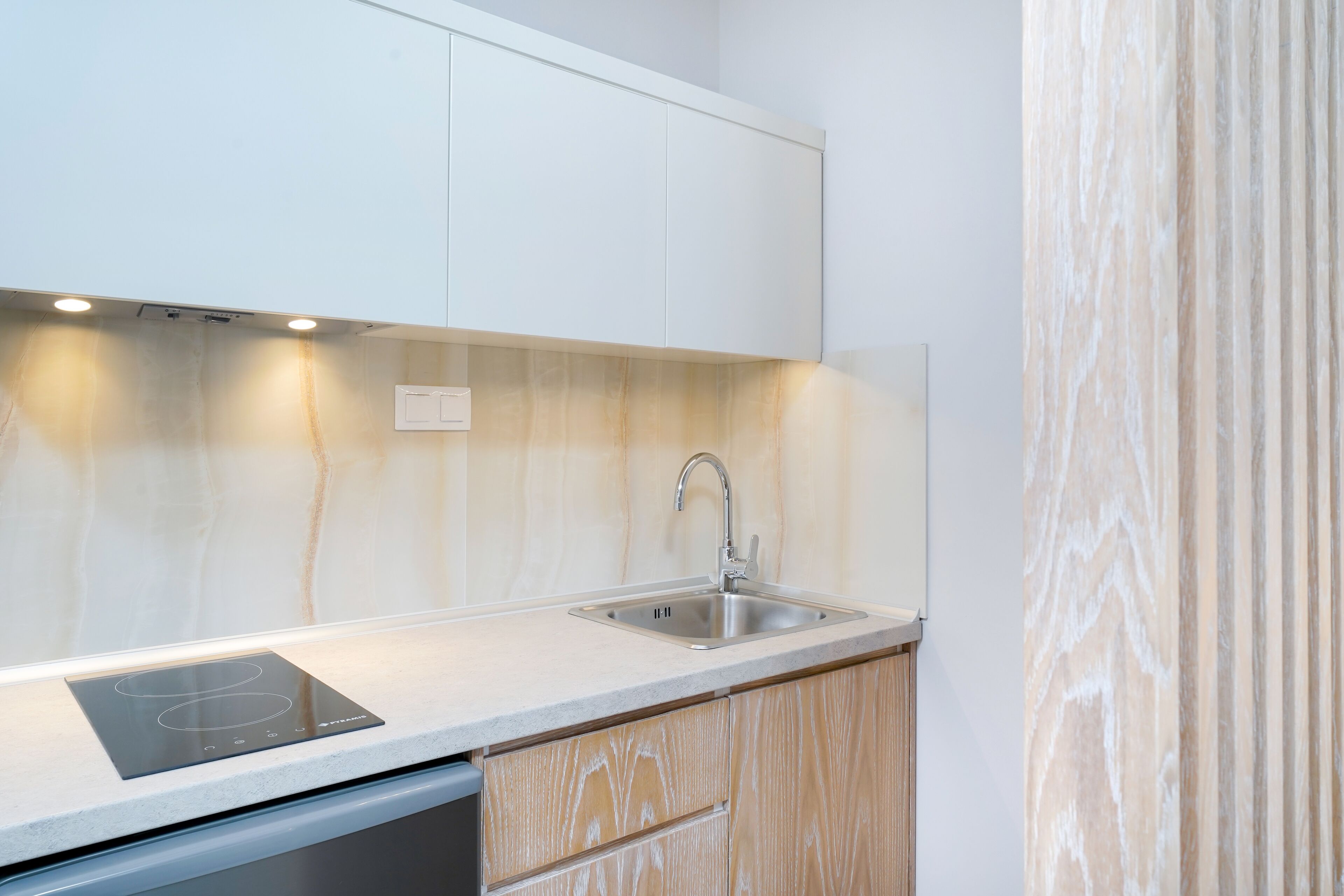 A modern kitchen with a built-in induction cooktop, stainless steel sink, and wooden cabinetry.