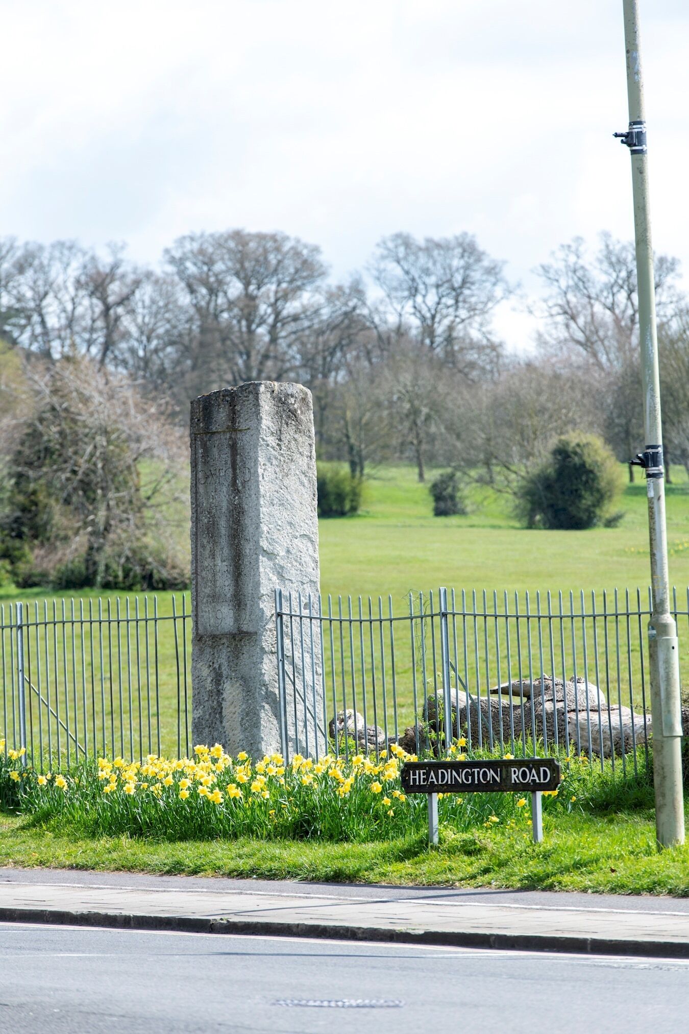Un pilier de pierre surmonté d’une clôture métallique, devant un panneau de signalisation indiquant « Headington Road ».