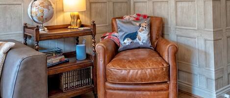 Un salon chaleureux avec un fauteuil en cuir, une table d’appoint en bois sur laquelle reposent un globe terrestre et une lampe, une bibliothèque et un tapis à motifs.