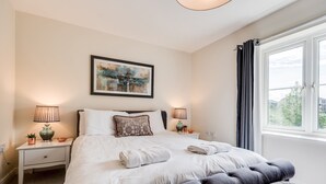 Een netjes ingerichte slaapkamer met een groot bed, twee bedlampen, een lijstwerk met een kunstwerk aan de muur en een raam met gordijnen.