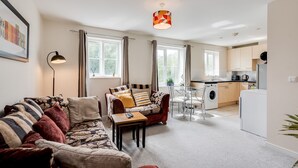 Een moderne woonkamer met een bank, een salontafel en een eethoek. Er is een keuken met een wasmachine en een eettafel.