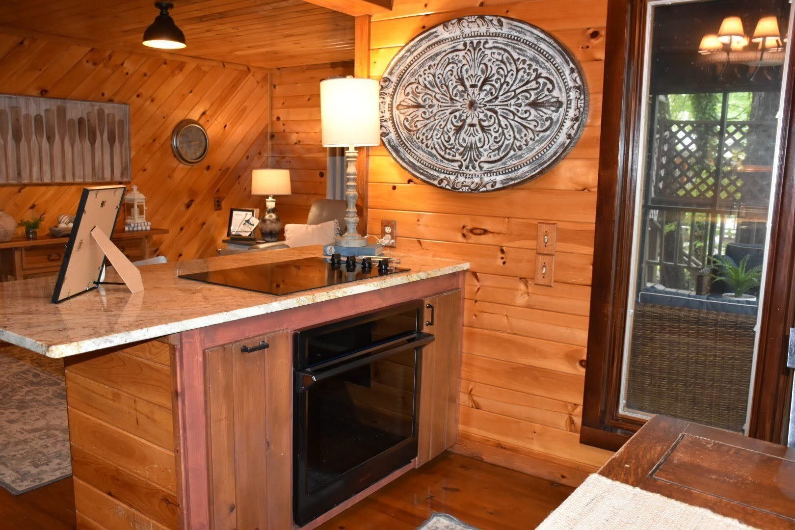 Una cocina con paredes de madera, horno empotrado, lavamanos y un plato decorativo en la pared.