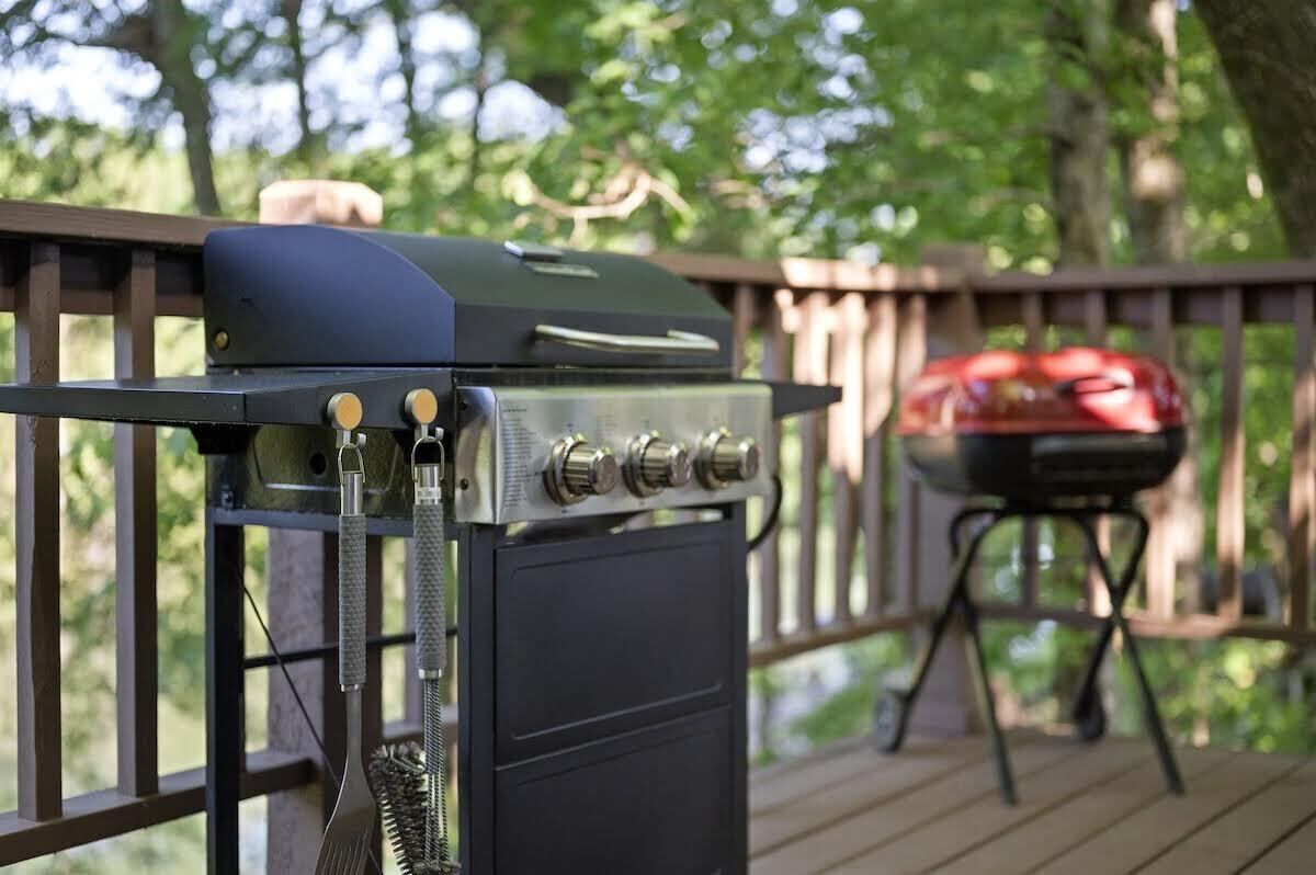 Un barbecue sur une terrasse en bois, avec un panier à griller et une housse de protection pour le barbecue en arrière-plan.