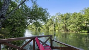 Eine Holzterrasse mit Geländer, die einen ruhigen Fluss mit üppiger Vegetation überblickt.