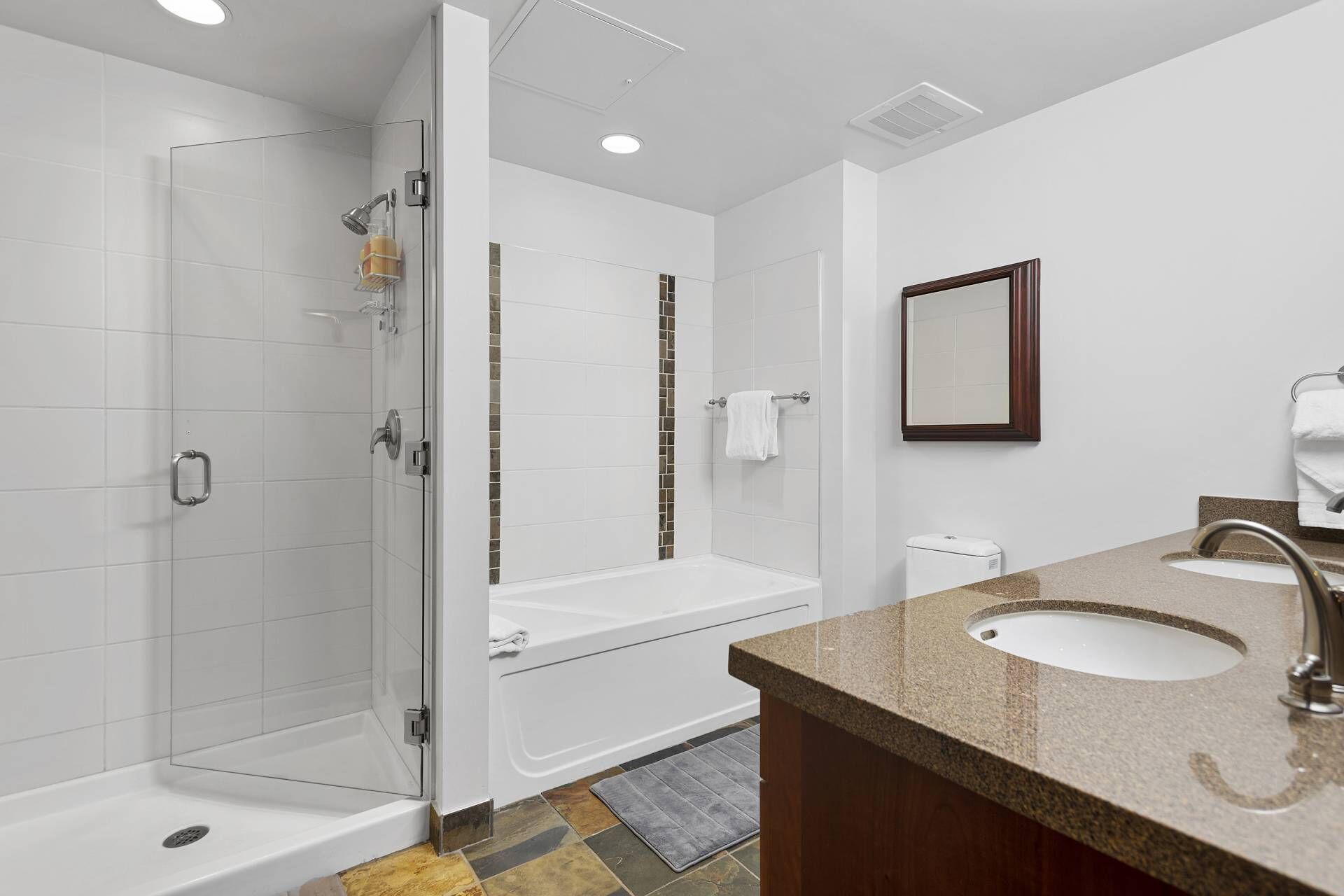 A modern bathroom with a glass-enclosed shower, a white bathtub, and a granite countertop with a sink.