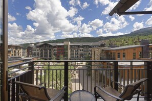 A balcony with chairs and a table overlooking a residential area with multi-story buildings and a mountainous backdrop. - Capitol Peak Lodge by iTrip Aspen Snowmass (Snowmass Village)