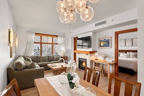 A modern living room with a sofa, dining table, and chairs, a fireplace, and a TV mounted on the wall. - Capitol Peak Lodge by iTrip Aspen Snowmass (Snowmass Village)