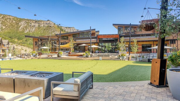 Un espace extérieur aménagé en terrasse, avec des sièges, un foyer et une vue sur un bâtiment portant l’inscription « Collective ».