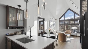 Une cuisine moderne dotée d’un grand îlot central, de luminaires suspendus et offrant une vue sur l’extérieur grâce à de grandes fenêtres.