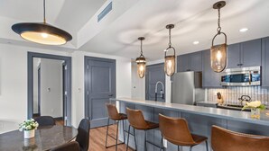Une cuisine moderne dotée d’un îlot central, de tabourets de bar, de luminaires suspendus et d’un four à micro-ondes.