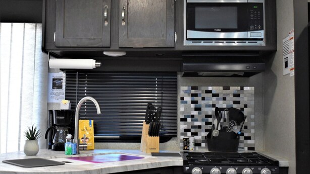 A modern kitchen with dark cabinets, a stainless steel microwave, a gas stove, and a tiled backsplash. - Grand Canyon RV Glamping Luxury Suite (Glamping Getaway) (Williams)