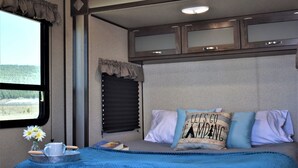 A cozy bedroom with a large window, a bed with blue and white bedding, and a tray with a cup and flowers. - Grand Canyon RV Glamping Luxury Suite (Glamping Getaway) (Williams)