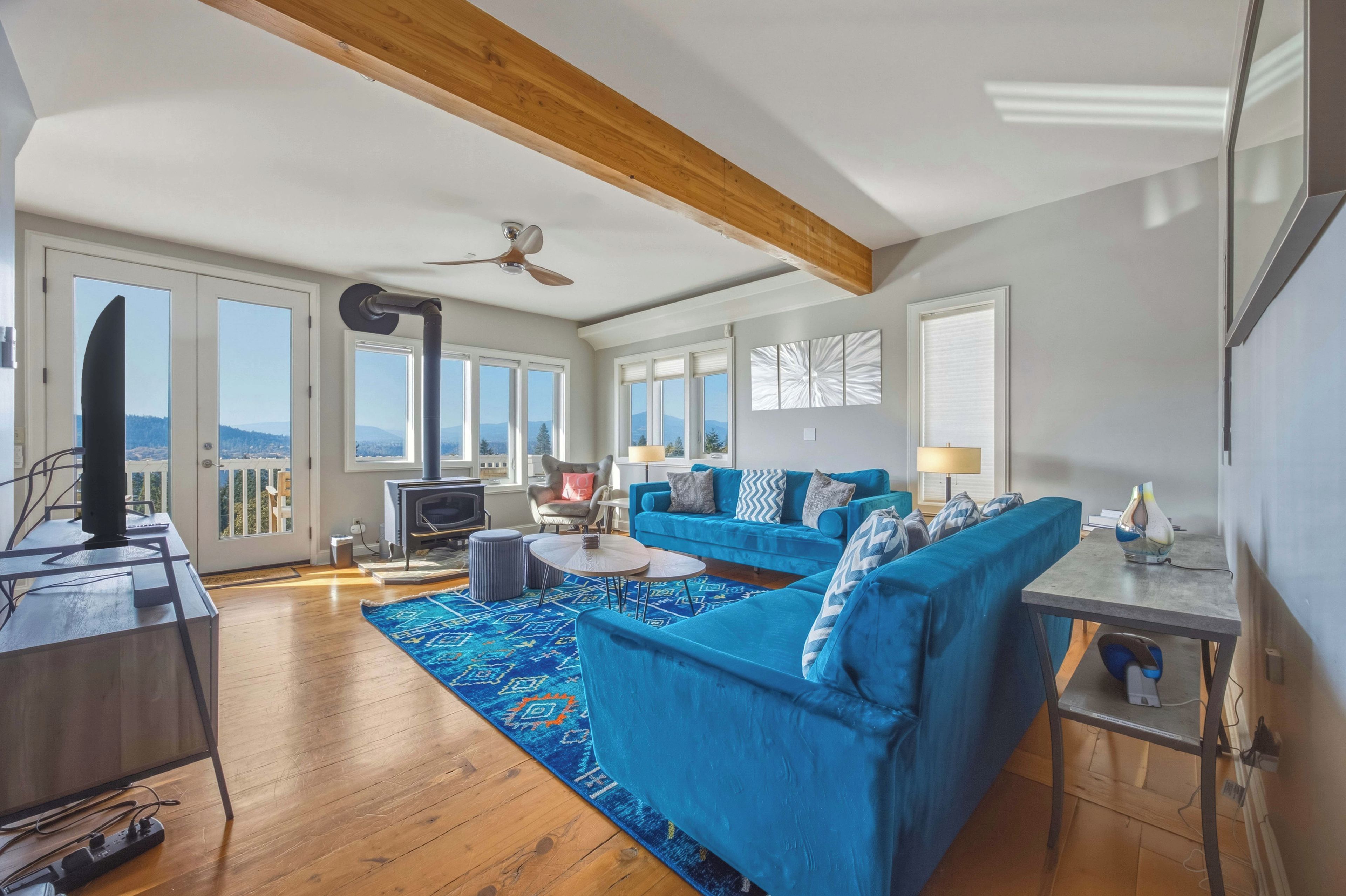 A spacious living room with a large blue sofa, a wooden ceiling, and a view through the large windows.