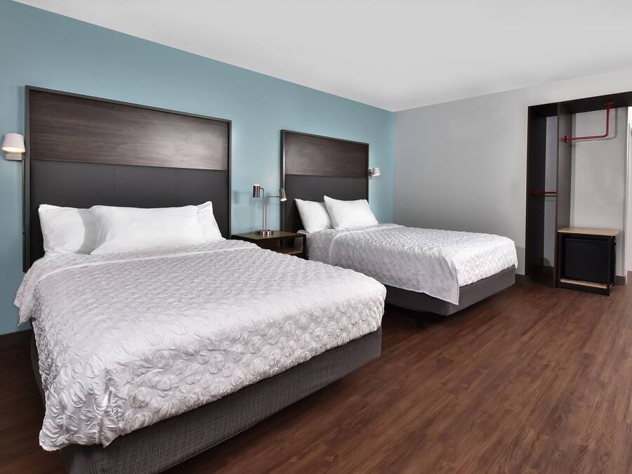 Una habitación de hotel con dos camas, piso de madera oscura y paredes azul claro.